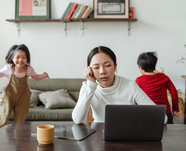 A parent trying to work at a laptop while two children run past
