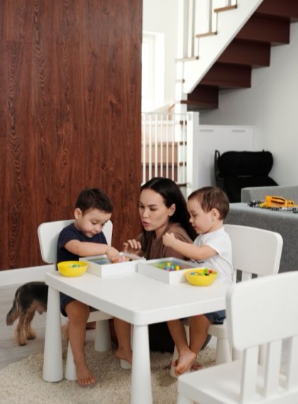 Au pair helping two toddlers with lunch at a small table