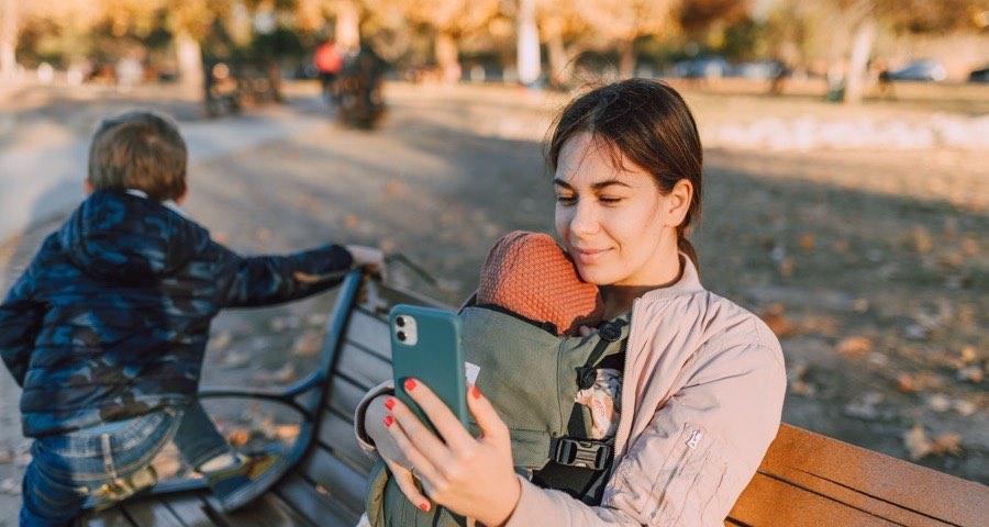 Au pair on a park bench checking her phone while minding two children